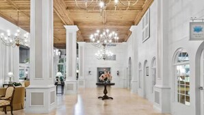 A spacious hallway with a wooden ceiling and chandeliers, white walls, and a central table with flowers.