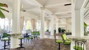 A spacious indoor area with high ceilings, white columns, and green cushioned chairs arranged around a central bar area. - TROPICAL PALM BEACH SUITE- 3 BEDS 2BEDROOMS 2BATHS POOL,BEACH,FRONT DESK 24/7 (PALM BEACH)