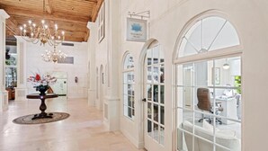 A spacious hallway with a chandelier, arched windows, and a sign indicating 'Palm Beach'.