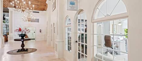 Un vestíbulo espacioso con candelabro, ventanas arqueadas y un letrero que indica 'Palm Beach'.
