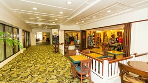 Un hall de hotel con alfombra estampada, mobiliario de madera y vista a una zona comercial.