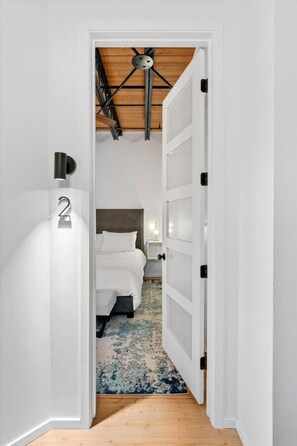 A narrow hallway leading to a bedroom with a bed, a number '2' sign, a ceiling fan, and a wooden floor. - Spacious 4BR Downtown Rooftop Loft (Denver)