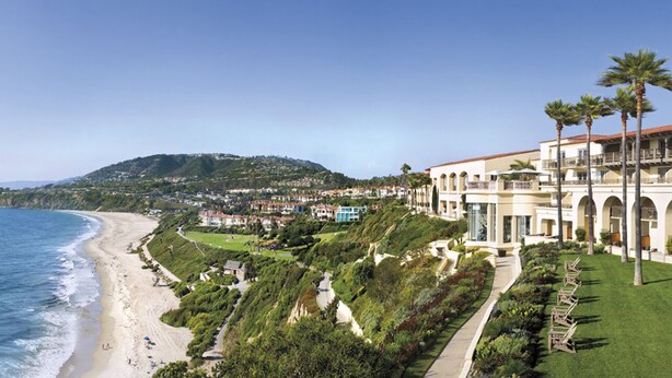 Ein Küstenhotel mit Blick auf den Strand, einem angelegten Garten und einem Hügel im Hintergrund.