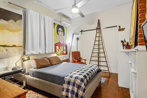 Een slaapkamer met een bed, een bureau, een stoel, een ladder en een schilderij aan de muur.