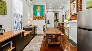 A modern kitchen with a dining area, featuring a wooden table, chairs, and a large painting on the wall. - Art Gem In Historic District Of New Orleans, cozy and elegant (New Orleans)