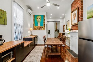 A modern kitchen with a dining area, featuring a wooden table, chairs, and a large painting on the wall. - Art Gem In Historic District Of New Orleans, cozy and elegant (New Orleans)