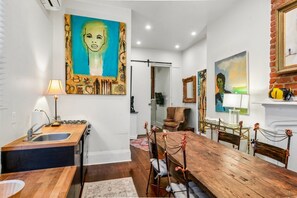 Een eetgedeelte met een houten tafel en stoelen, een keuken met een spoelbak en fornuis, en kunstwerken aan de wanden.