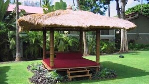 A thatched gazebo with a red floor, surrounded by lush greenery and palm trees. - Aina Nalu Studio, Great Rates & Location, AC & WIFI,  2 Pools & Jacuzzi (Lahaina)