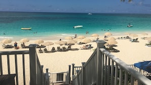A beach with clear turquoise water, a sandy shore, and several umbrellas and lounge chairs.