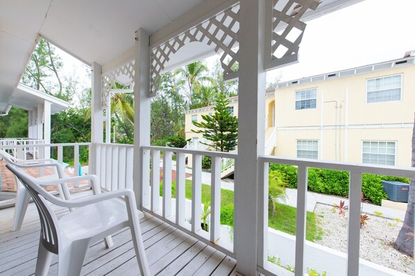 A covered outdoor area with white plastic chairs and a white railing.