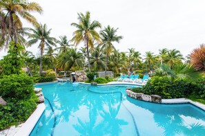 Una piscina con agua azul, rodeada de palmeras y sillas de descanso.