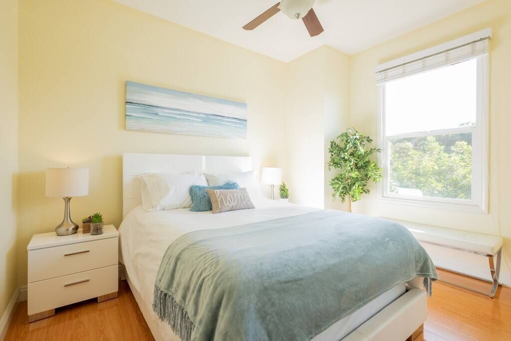 Una camera da letto con un letto, lampade sui comodini, una ventola a soffitto, una finestra con vista e un quadro appeso al muro.