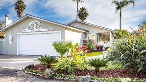 A single-story house with a white garage door, a decorative roofline, and a well-maintained front yard with various plants and a small garden area.