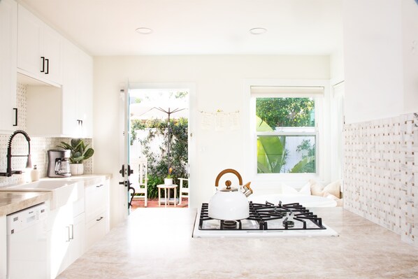 A modern kitchen with white cabinets, a gas stove, and a view of the garden through the window. - Adorable Octopus Hideaway: 2 min walk to the beach! (Del Mar)