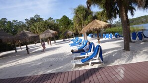 Una playa con sombrillas de paja, tumbonas y palmeras.