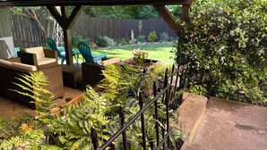 A covered patio area with outdoor furniture, a garden with ferns, and a view of a backyard with a wooden fence. - Pet friendly apartment with covered patio and fenced-in yard. (Portland)