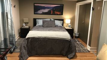 Un dormitorio ordenado con una cama grande, dos mesitas de noche con lámparas, un cuadro en la pared y una puerta a la derecha.