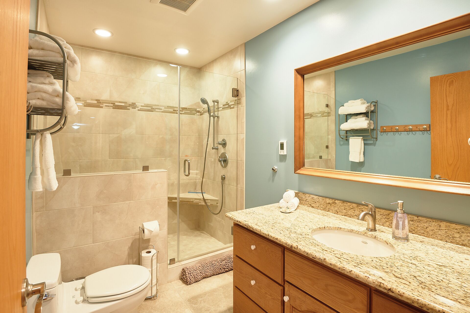 A bathroom with a glass-enclosed shower, a sink with a granite countertop, and a mirror with a wooden frame.