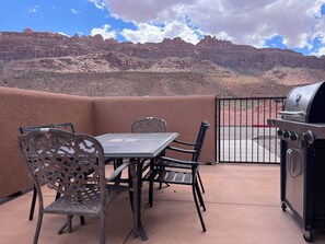 Un patio al aire libre con una mesa, sillas, una parrilla y vistas a un paisaje montañoso.