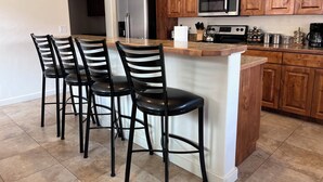 A kitchen with wooden cabinets, a stainless steel refrigerator, a microwave, and a gas stove. There are four black chairs with white stripes around a central island.