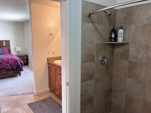 A bathroom with a shower, a sink, and toiletries on a shelf.