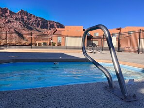 A swimming pool with a metal ladder, a desert landscape, and a building in the background.