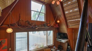 A cozy loft-style room with a large window, a television, and a ceiling fan.
