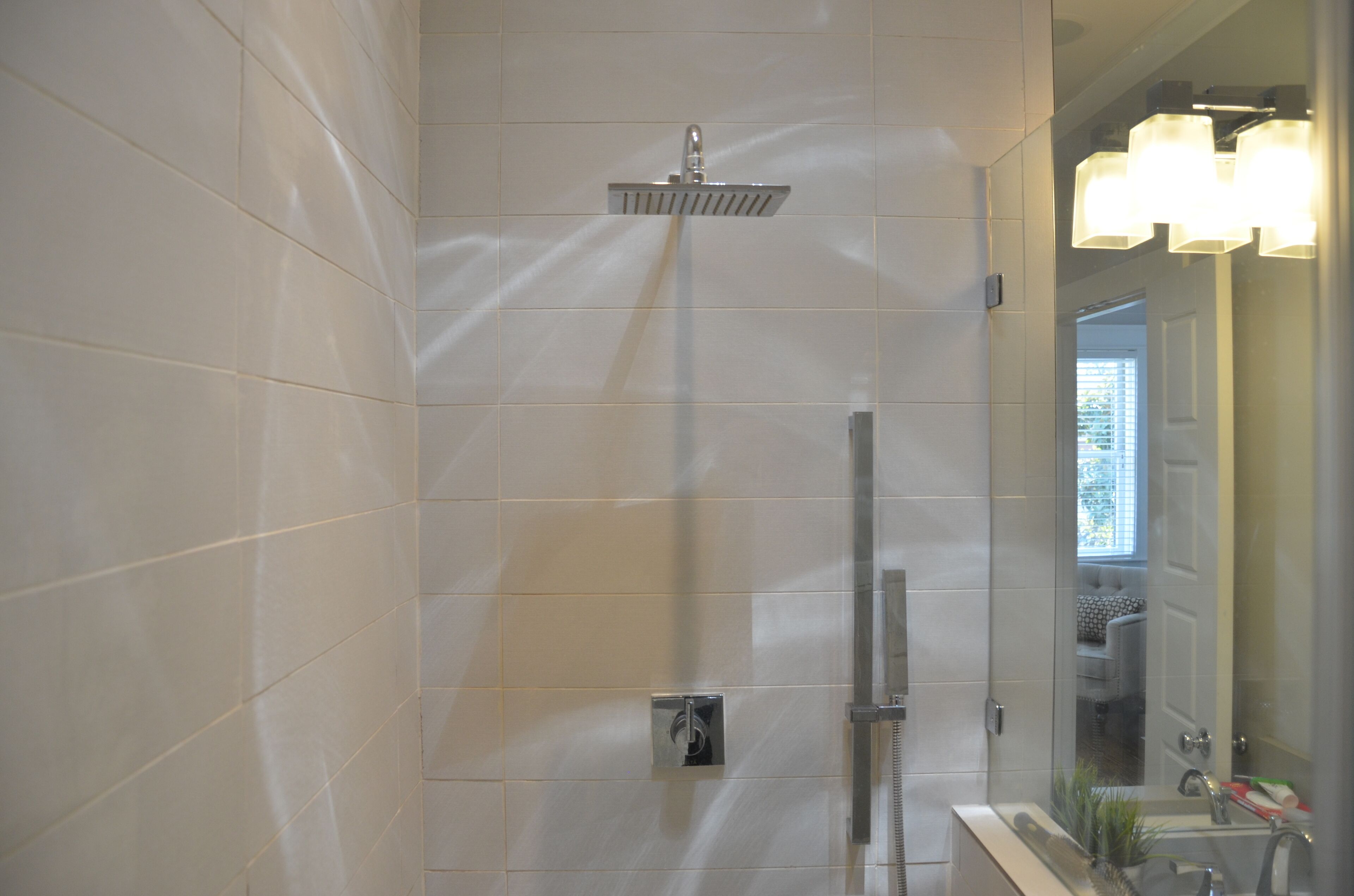 A modern bathroom with white tiles, a shower, a sink, and a mirror.