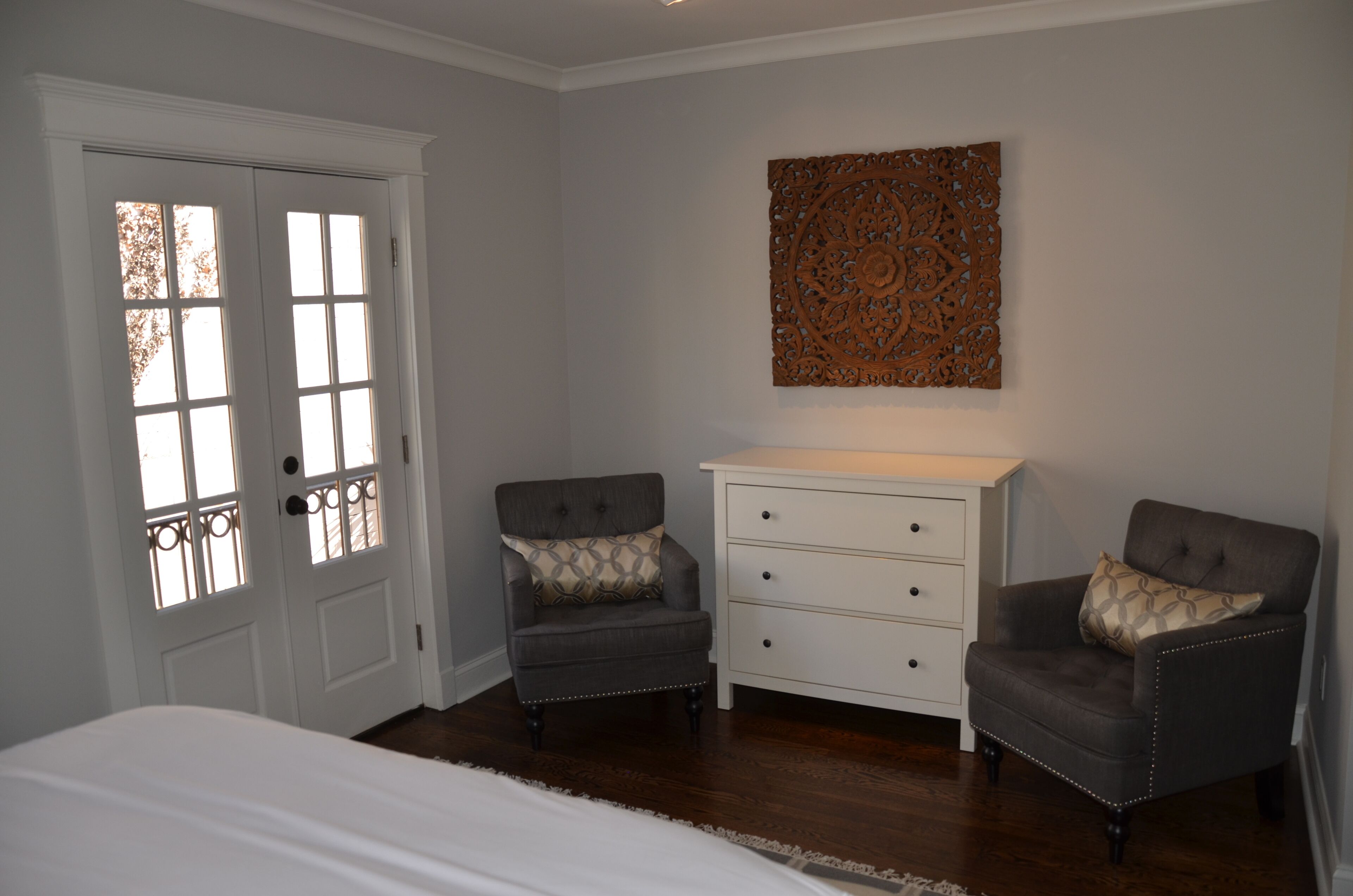 Een slaapkamer met een bed, twee fauteuils, een kaptafel en een decoratief wandobject.