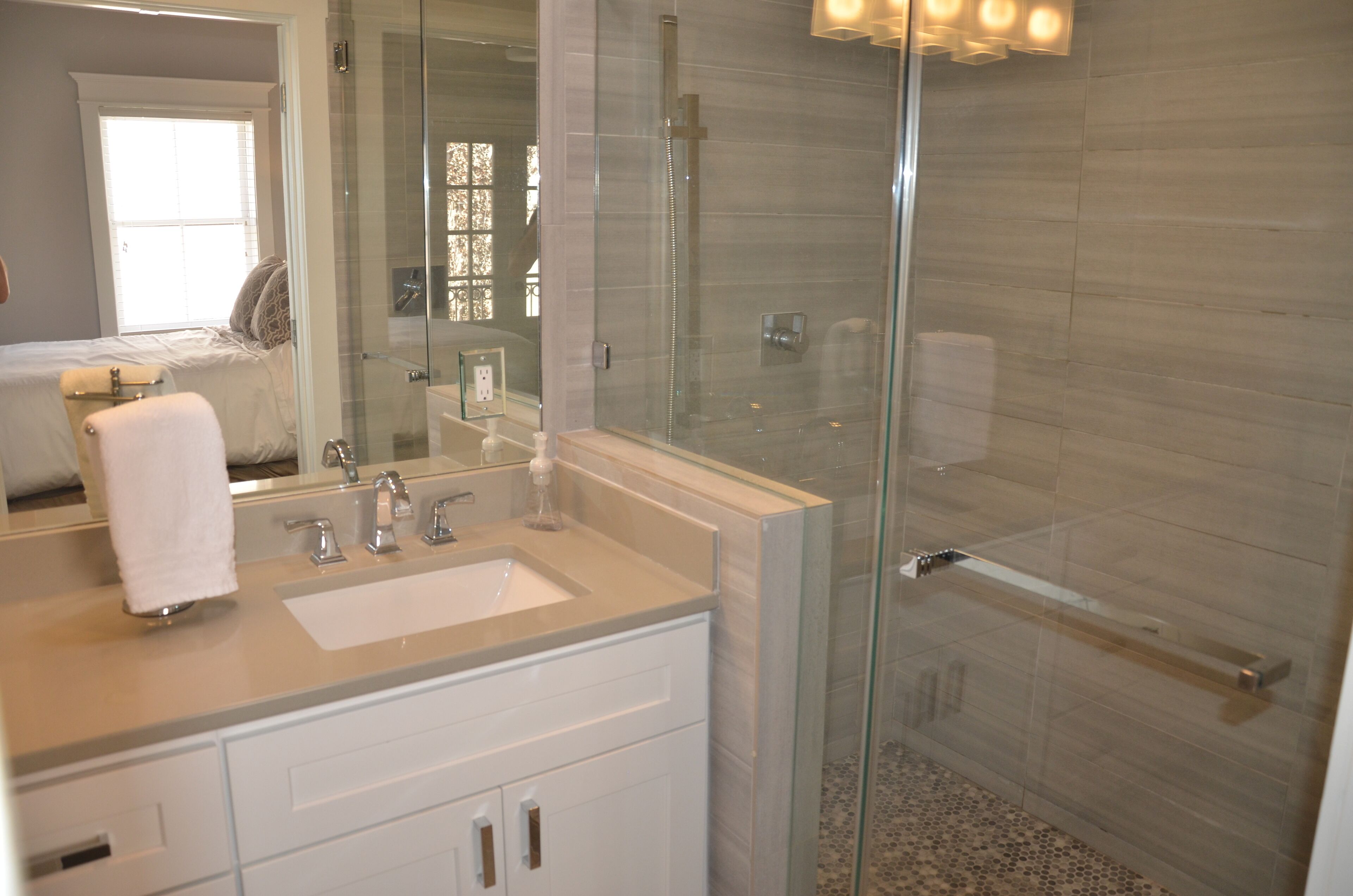 A modern bathroom with a glass-enclosed shower, a large mirror, and a vanity with a sink and cabinets.