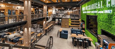 A spacious indoor area with multiple seating arrangements, a visible staircase, and a green wall with signage.