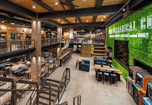 A spacious indoor area with multiple seating arrangements, a visible staircase, and a green wall with signage.