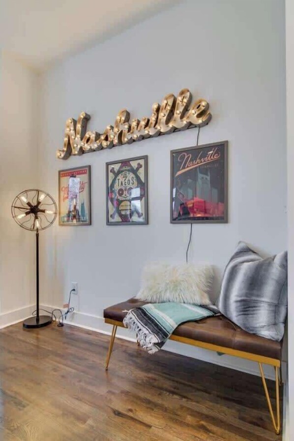 Um quarto com um sofá de couro marrom, uma placa na parede com a inscrição 'Nashville' e três pôsteres emoldurados.