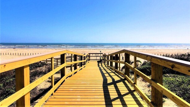 A wooden boardwalk leading to a beach with a clear view of the ocean.