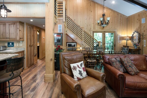 Un vaste espace de vie comprenant un grand canapé en cuir marron, un escalier en bois et un coin repas avec des meubles en bois.