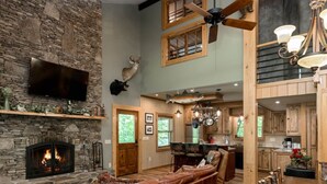 Ein großzügiges Wohnzimmer mit Kamin aus Stein, einer Ledersofa und einem Essbereich mit Holztischen und -stühlen.