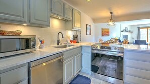 A modern kitchen with stainless steel appliances, white cabinetry, and a dining area with wooden chairs. - Remodeled Condo Near Slopes, Pool/Hot Tub Access! (Silverthorne)
