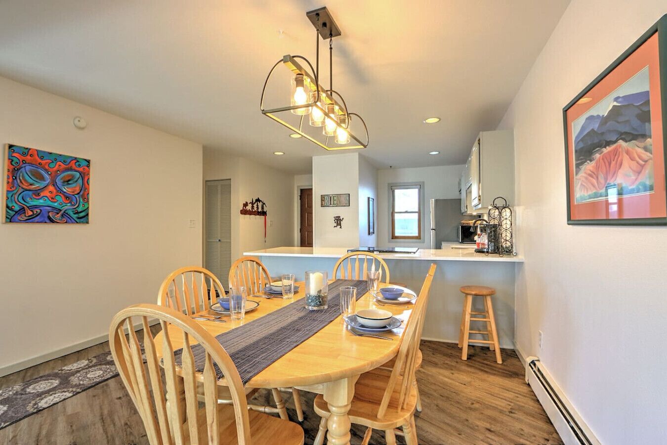 A dining area with a wooden table and chairs, a modern pendant light, and a kitchen in the background.