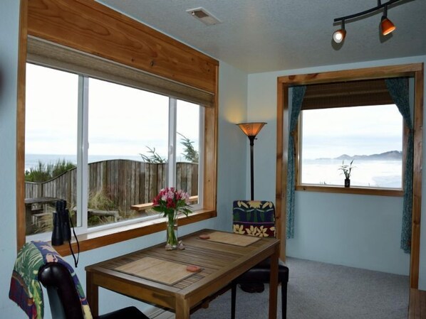 A room with a wooden table, a lamp, and a view of the ocean. - Ocean Wind Retreat, Oceanfront, romantic, ideal for couples, pet friendly (Newport)