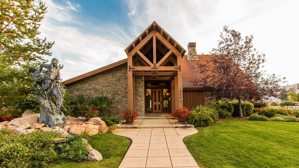 A stone building with a wooden entrance and a statue in the garden. - Big Piney Family Fun (Eden)