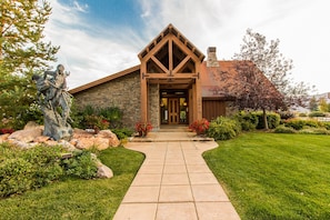 A stone building with a wooden entrance and a statue in the garden. - Big Piney Family Fun (Eden)