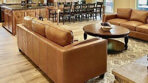 A spacious living area with a large leather sofa, a dining table with chairs, and a kitchen area with wooden cabinets and a chandelier. - Big Piney Family Fun (Eden)