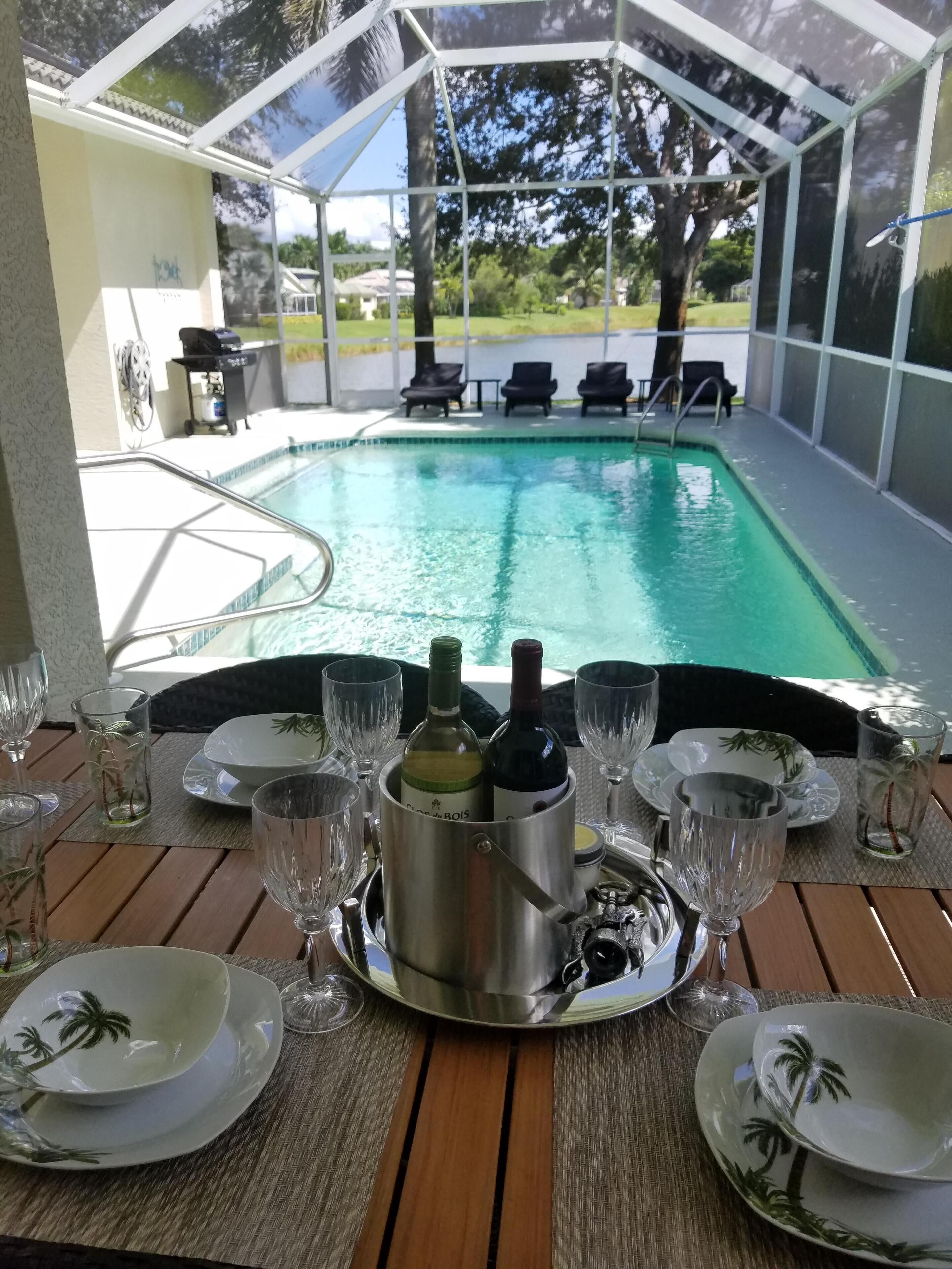 Ein Tisch am Pool mit einem Metallkübel voller Flaschen, umgeben von Tellern, Schalen und Weingläsern.