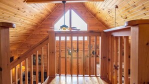 Un intérieur en bois avec un plafond en pente, un ventilateur de plafond au centre et une vue sur l’extérieur par une fenêtre.