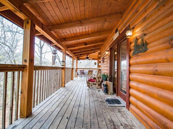 Une cabane en bois dotée d’un porche couvert, d’un ventilateur de plafond et offrant une vue sur les arbres environnants.