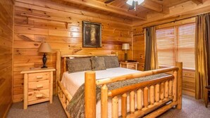 Une chambre à coucher dans une cabane en bois, avec un lit, deux tables de chevet, un ventilateur de plafond et une fenêtre avec des rideaux.