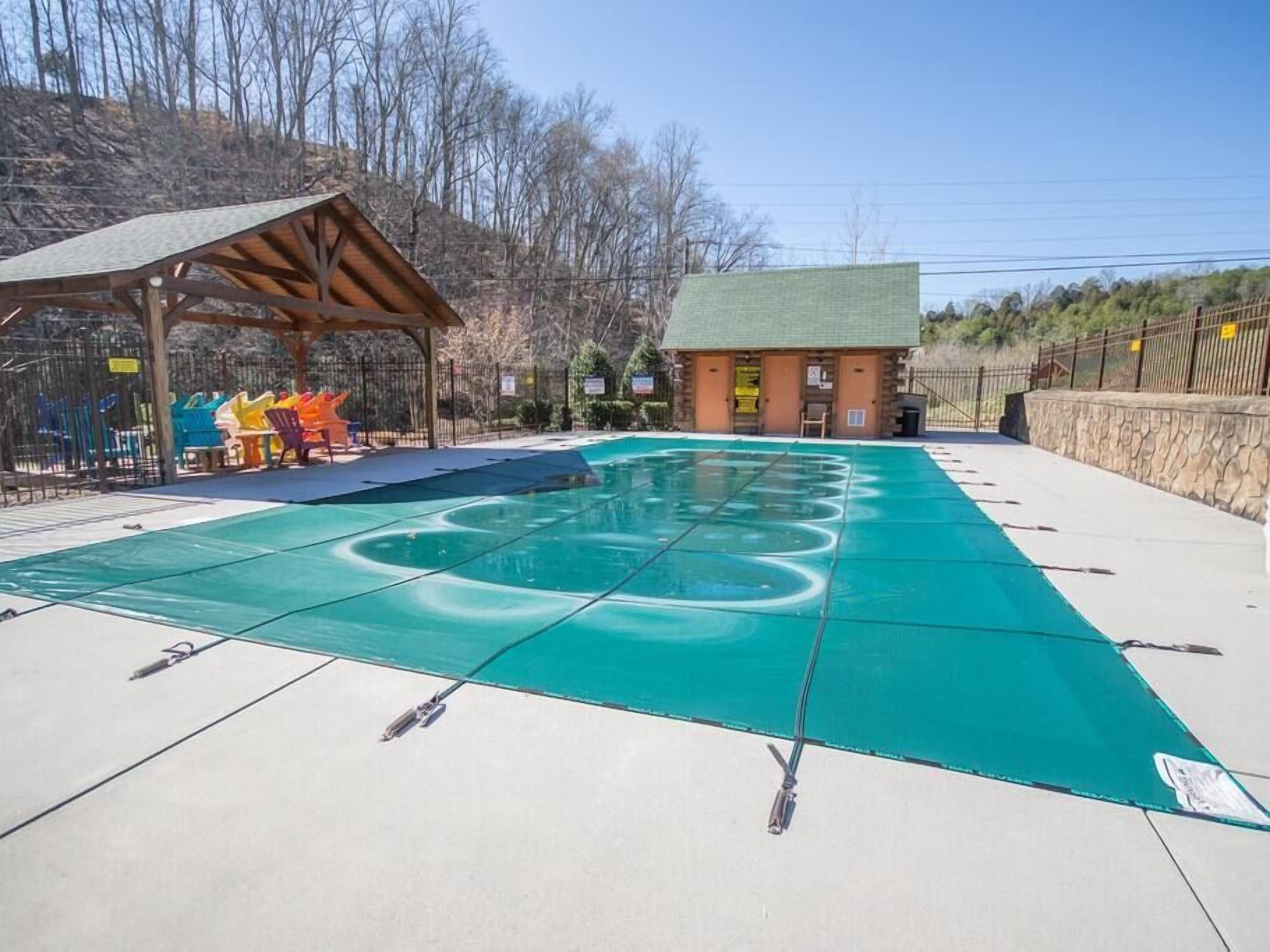 A swimming pool with a green cover, a wooden pavilion, and a small building with a green roof.