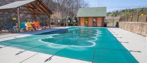 A swimming pool with a green cover, a wooden pavilion, and a small building with a green roof.