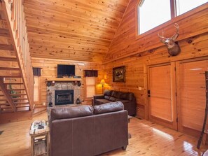 L’intérieur d’une cabane en rondins, avec une cheminée, un canapé en cuir et une tête de cerf accrochée au mur.