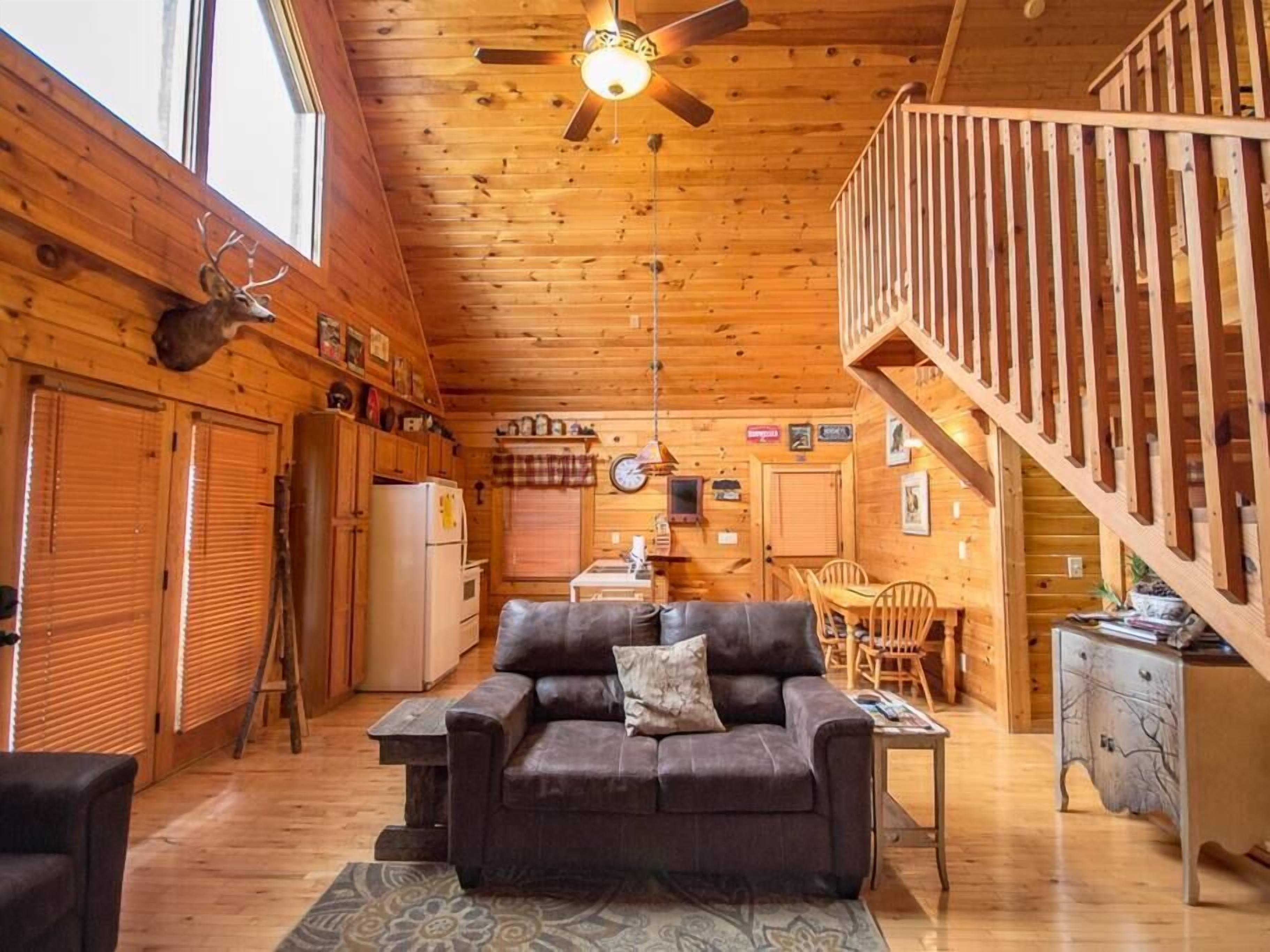 L’intérieur chaleureux d’un chalet avec un plafond en bois, un coin repas, un canapé et un escalier.